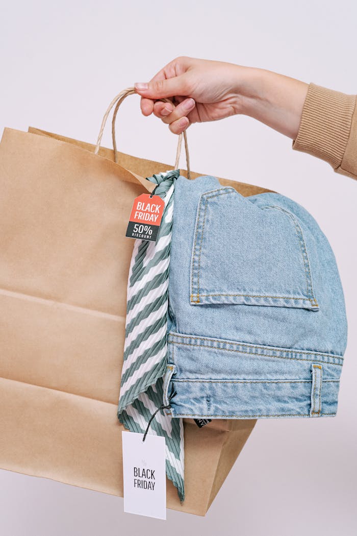 Close-up of a hand holding a shopping bag with denim jeans, perfect for Black Friday sales.