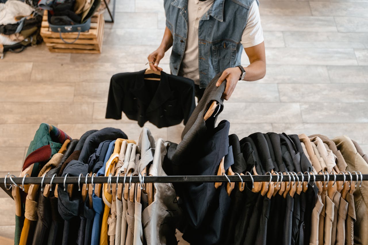 journey-01 A person holds a jacket while organizing clothes on a rack in a stylish boutique.